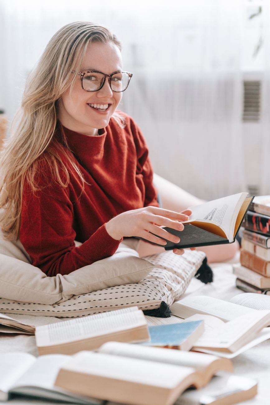 Smiling woman with glasses reading in a cozy indoor setting